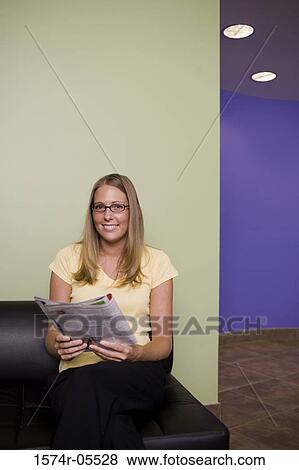 Stock Photo - Portrait of a businesswoman sitting on a couch holding a magazine. Fotosearch