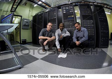 Stock Photograph - Portrait of three technicians crouching in front of a network server. Fotosearch