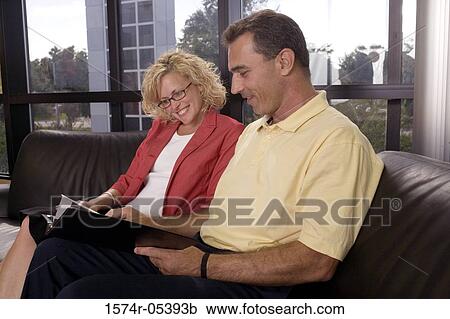Side profile of a businessman and a businesswoman sitting on a couch reading a document View Large Photo Image Stock Image - Side profile of a businessman and a businesswoman sitting on a couch reading a document. Fotosearch
