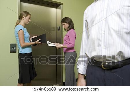 Side profile of two businesswomen reading documents while waiting for an elevator View Large Photo Image Stock Photo - Side profile of two businesswomen reading documents while waiting for an elevator. Fotosearch