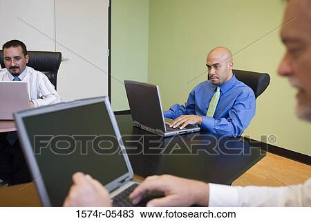 Stock Image - Three businessmen working on laptops in a conference room. Fotosearch