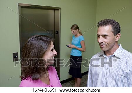 Stock Image - Two businesswomen and a businessman waiting for an elevator. Fotosearch