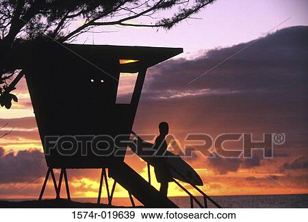 Stock Photo - Silhouette of a young man with a surfboard on the steps of a lifeguard hut. Fotosearch