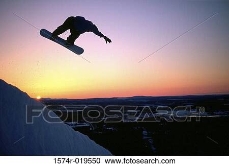 Stock Image - Silhouette of person performing stunt on snowboard. Fotosearch
