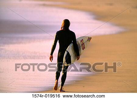 Surfer walking along the beach View Large Photo Image Stock Photograph - Surfer walking along the beach. Fotosearch