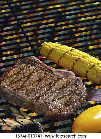 Stock Photo - Close-up of a piece of meat and corn on the cob cooking on a grill. Fotosearch