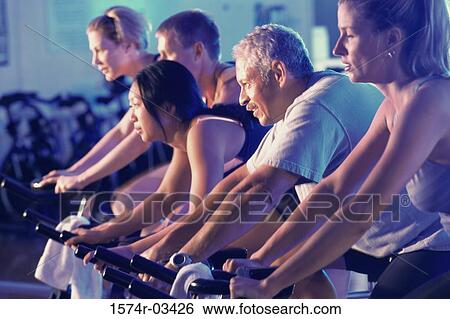 Stock Photograph - Group of people on exercise bikes in a health club. Fotosearch