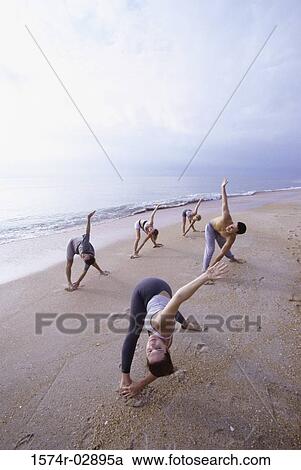 Stock Image - Group of people performing yoga on the beach. Fotosearch