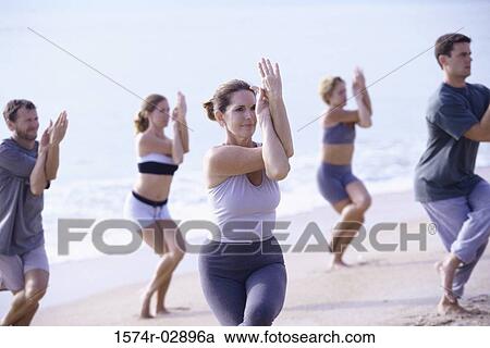 Stock Image - Group of people performing yoga on the beach. Fotosearch