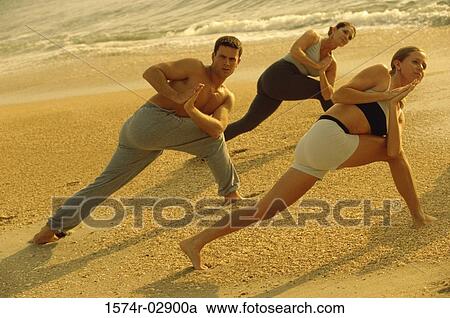 Stock Image - Group of people performing yoga on the beach. Fotosearch