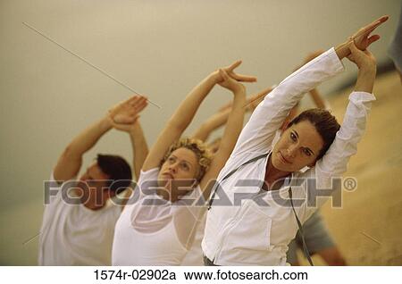 Stock Image - Group of people performing yoga on the beach. Fotosearch