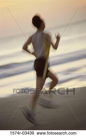 Stock Photo - Rear view of a mid adult man jogging on the beach. Fotosearch