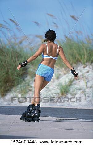 Rear view of a young woman inline skating on road View Large Photo Image Stock Photo - Rear view of a young woman inline skating on road. Fotosearch