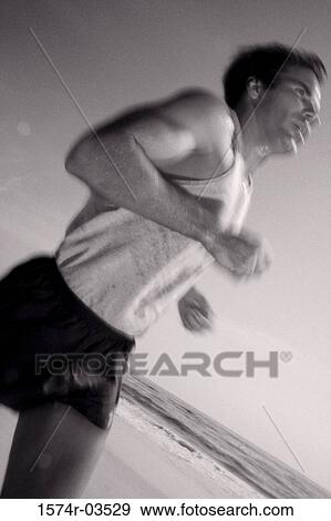 Stock Photo - Side profile of a young man jogging on the beach. Fotosearch