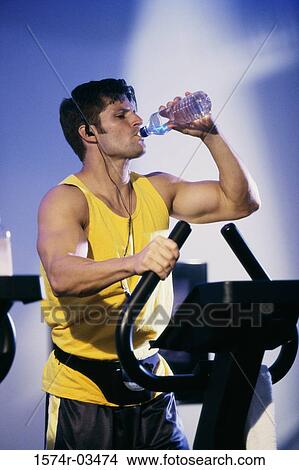 Picture - Young man drinking water during exercise. Fotosearch
