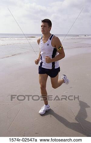 Stock Image - Young man jogging on the beach. Fotosearch
