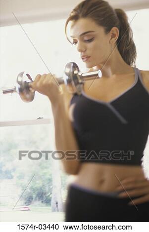Stock Image - Young woman exercising with dumbbells. Fotosearch