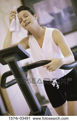 Stock Image - Young woman standing on a treadmill in a health club. Fotosearch
