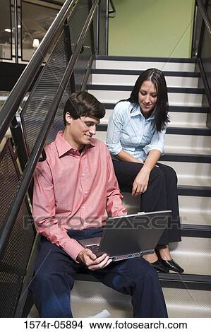 Businessman and a businesswoman sitting on stairs in front of a laptop View Large Photo Image Picture - Businessman and a businesswoman sitting on stairs in front of a laptop. Fotosearch
