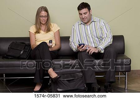 Businessman and a businesswoman sitting on a couch holding mobile phones View Large Photo Image Stock Image - Businessman and a businesswoman sitting on a couch holding mobile phones. Fotosearch