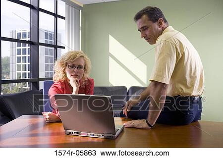 Businessman and a businesswoman sitting in front of a laptop View Large Photo Image Stock Image - Businessman and a businesswoman sitting in front of a laptop. Fotosearch