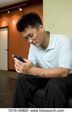 Stock Image - Businessman sitting in an office holding a mobile phone. Fotosearch