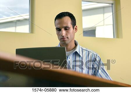 Stock Image - Businessman sitting in an office working on a laptop. Fotosearch