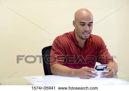 Businessman sitting in an office holding a palmtop View Large Photo Image Stock Image - Businessman sitting in an office holding a palmtop. Fotosearch