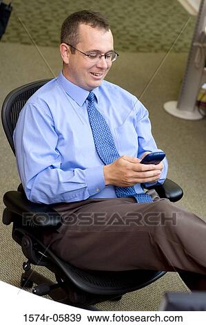 Businessman sitting in an office holding a palmtop View Large Photo Image Stock Photo - Businessman sitting in an office holding a palmtop. Fotosearch