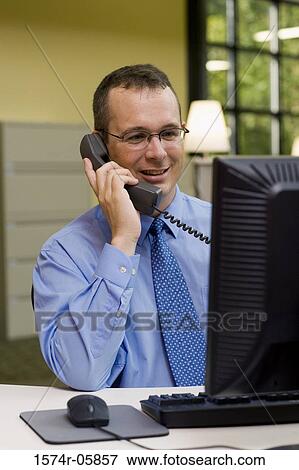 Businessman sitting in an office talking on a telephone View Large Photo Image Stock Photo - Businessman sitting in an office talking on a telephone. Fotosearch