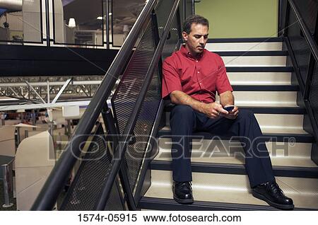 Businessman sitting on stairs holding a mobile phone View Large Photo Image Stock Photography - Businessman sitting on stairs holding a mobile phone. Fotosearch