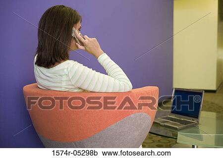 Stock Image - Businesswoman sitting in front of a laptop talking on a mobile phone. Fotosearch