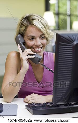 Businesswoman sitting in front of a computer talking on a telephone View Large Photo Image Stock Image - Businesswoman sitting in front of a computer talking on a telephone. Fotosearch