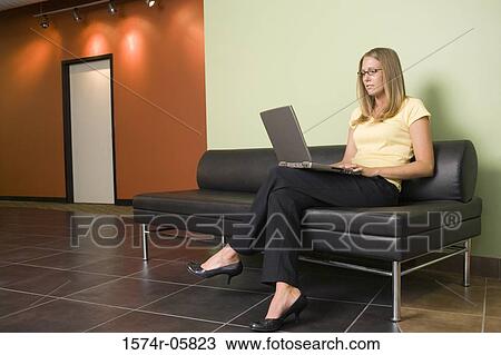 Businesswoman sitting on a couch working on a laptop View Large Photo Image Stock Image - Businesswoman sitting on a couch working on a laptop. Fotosearch
