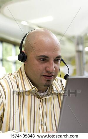 Close-up of a male customer service representative wearing a headset sitting in front of a laptop View Large Photo Image Stock Image - Close-up of a male customer service representative wearing a headset sitting in front of a laptop. Fotosearch