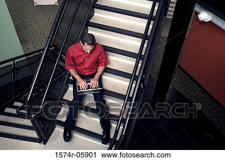 High angle view of a businessman sitting on stairs working on a laptop View Large Photo Image Stock Image - High angle view of a businessman sitting on stairs working on a laptop. Fotosearch