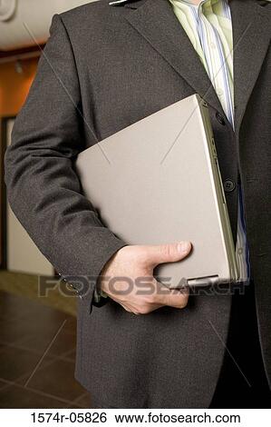 Stock Photograph - Mid section view of a businessman holding a laptop. Fotosearch