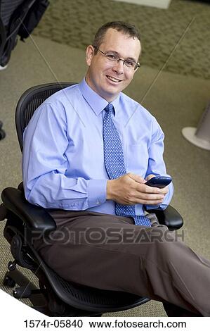 Portrait of a businessman sitting in an office holding a palmtop View Large Photo Image Stock Image - Portrait of a businessman sitting in an office holding a palmtop. Fotosearch