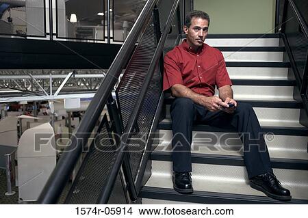 Portrait of a businessman sitting on stairs holding a mobile phone View Large Photo Image Picture - Portrait of a businessman sitting on stairs holding a mobile phone. Fotosearch