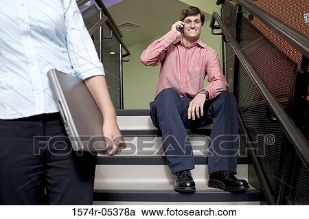 Stock Image - Portrait of a businessman sitting on stairs talking on a mobile phone. Fotosearch