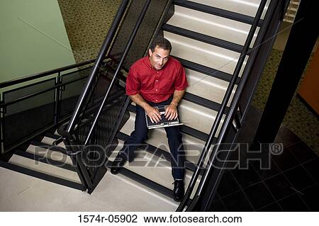Portrait of a businessman sitting on stairs working on a laptop View Large Photo Image Stock Image - Portrait of a businessman sitting on stairs working on a laptop. Fotosearch