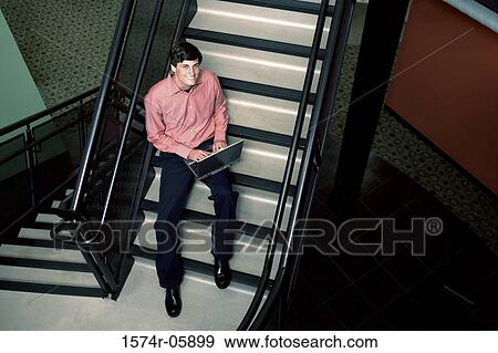 Stock Photo - Portrait of a businessman sitting on stairs working on a laptop. Fotosearch
