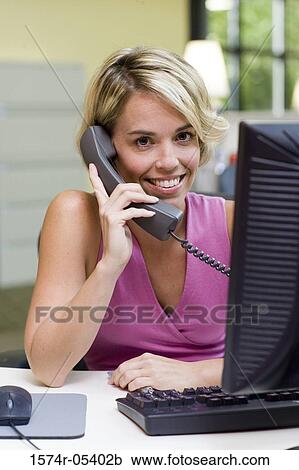 Stock Image - Portrait of a businesswoman sitting in front of a computer talking on a telephone. Fotosearch