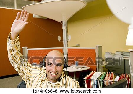 Stock Photo - Portrait of a male customer service representative wearing a headset with his hand raised. Fotosearch