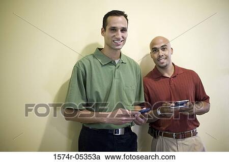 Portrait of two businessmen standing in an office holding palmtops View Large Photo Image Stock Image - Portrait of two businessmen standing in an office holding palmtops. Fotosearch