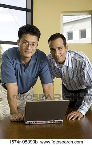 Portrait of two businessmen standing in front of a laptop View Large Photo Image Stock Image - Portrait of two businessmen standing in front of a laptop. Fotosearch