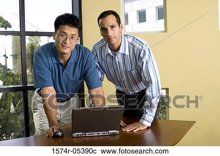 Portrait of two businessmen standing in front of a laptop View Large Photo Image Stock Image - Portrait of two businessmen standing in front of a laptop. Fotosearch