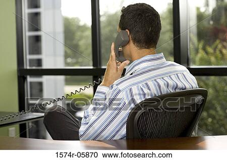 Rear view of a businessman sitting in an office using a telephone View Large Photo Image Stock Image - Rear view of a businessman sitting in an office using a telephone. Fotosearch