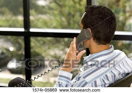 Rear view of a businessman sitting in an office using a telephone View Large Photo Image Stock Photo - Rear view of a businessman sitting in an office using a telephone. Fotosearch
