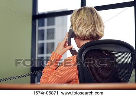 Stock Image - Rear view of a businesswoman sitting in an office talking on a telephone. Fotosearch